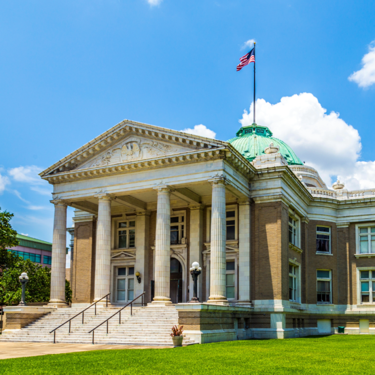 Historic courthouse building in downtown Lake Charles Louisiana featuring classical architecture, tall columns, and an American flag under a bright blue sky.